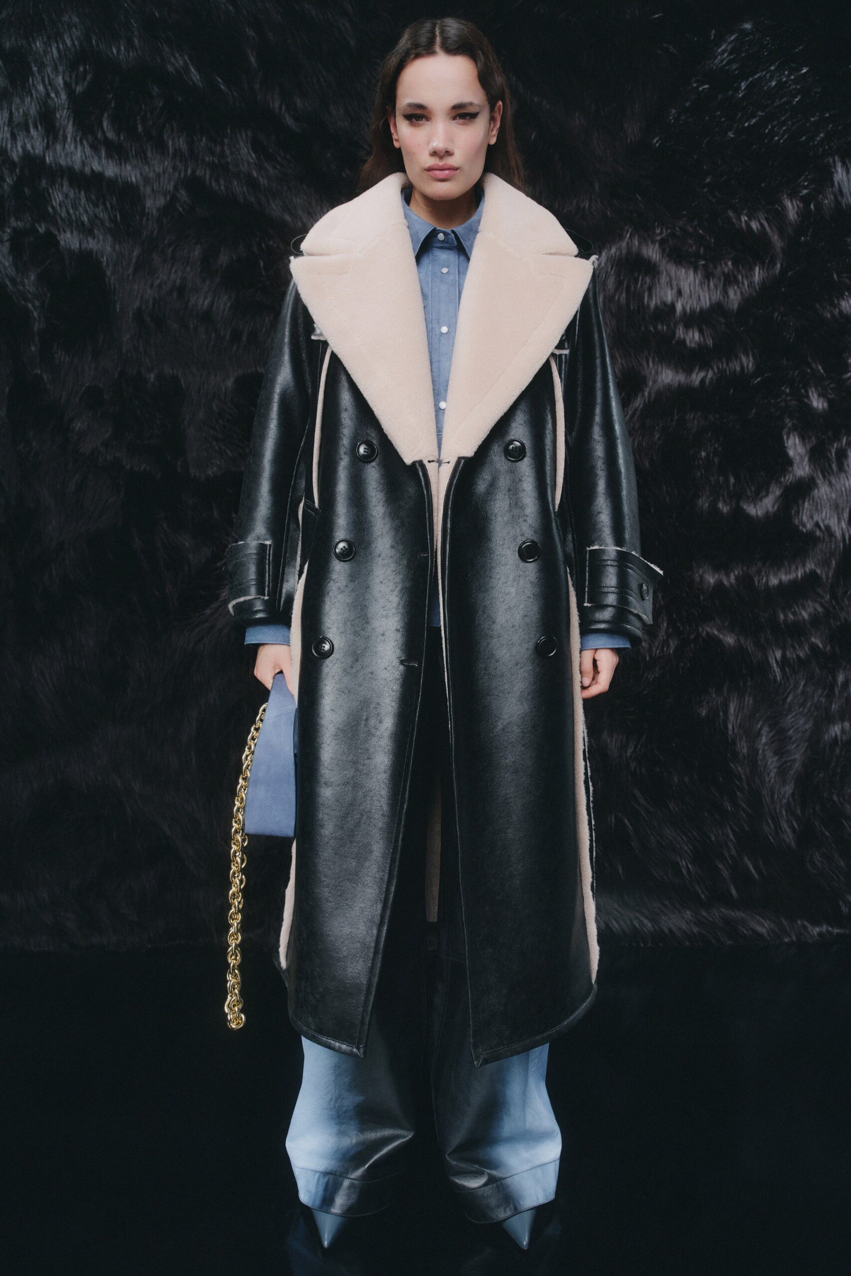 A relaxed black leather coat paired with blue denim pants featuring a collared design and buttoned detail.