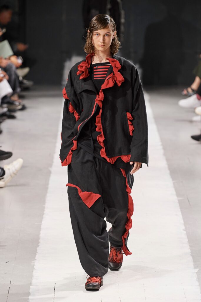 A relaxed black jacket with ruffled details paired with matching pants featuring red accents.