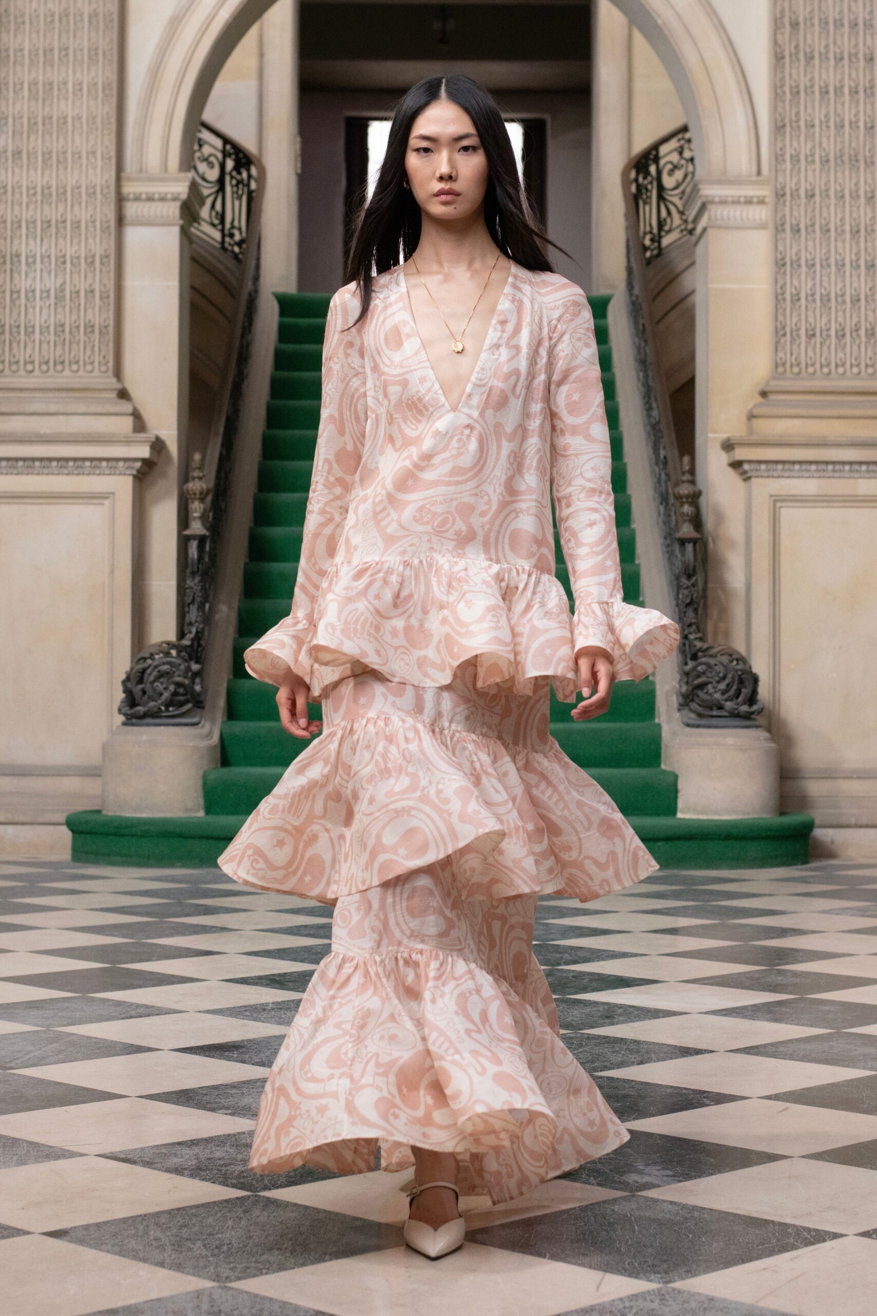 A fitted pink silk dress with a V-neckline and tiered design details.