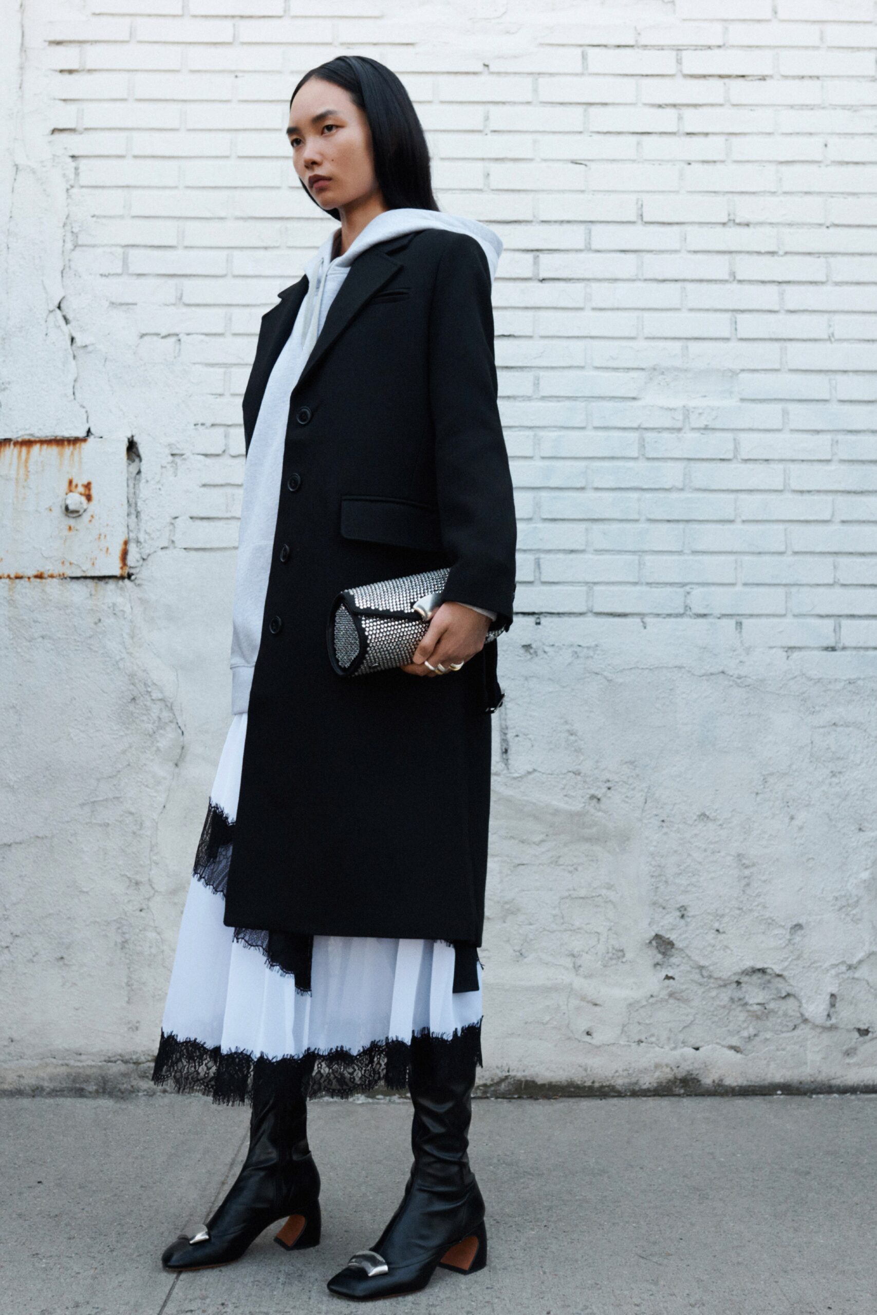 A fitted black coat layered over a white dress with fringed details.