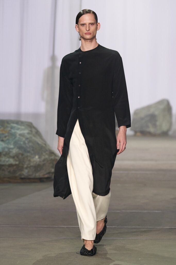 A relaxed black coat with long sleeves and a collared neckline, paired with white pants.