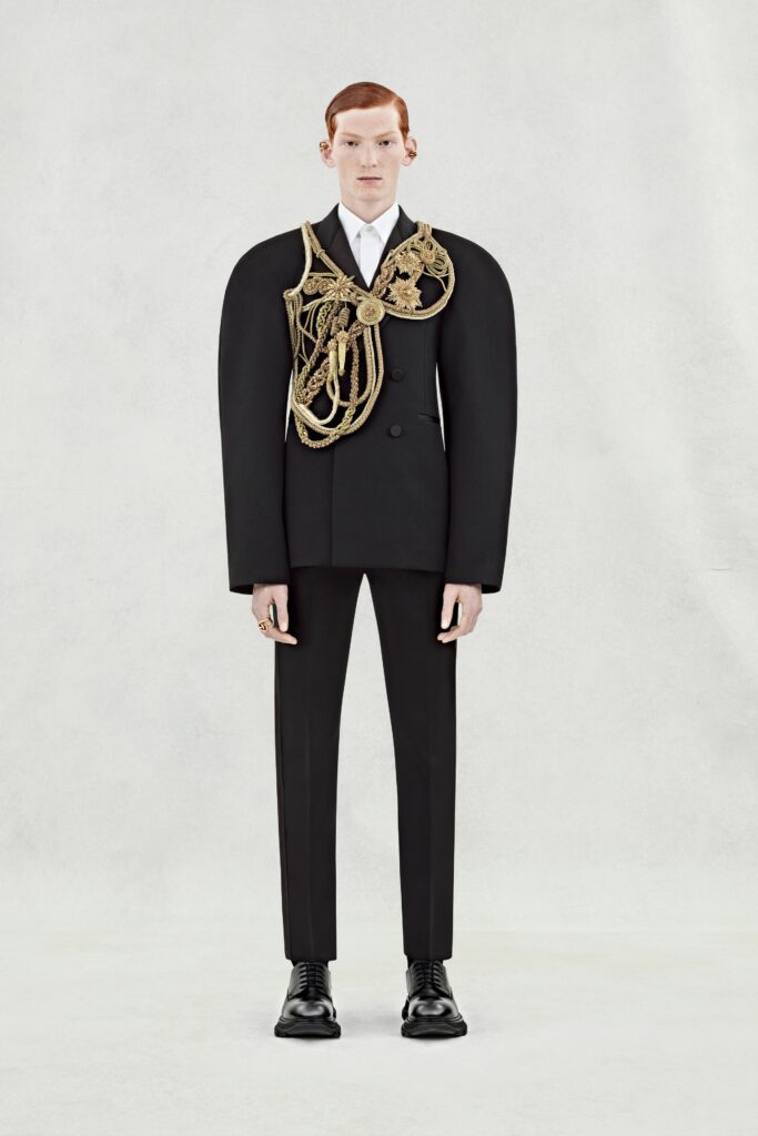 A tailored black suit with long sleeves, a collared shirt, and an asymmetric design detail.