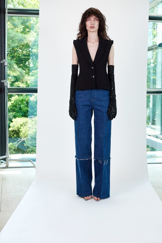 A fitted black sleeveless blazer paired with flared blue denim pants.