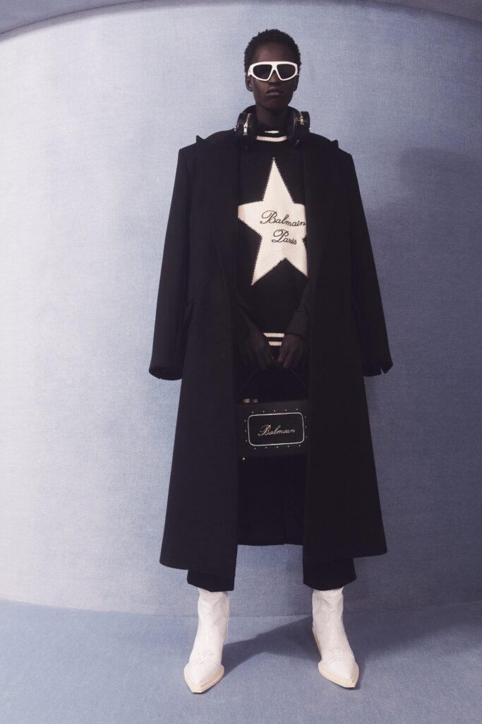 An oversized black coat layered over a white star-patterned sweater, creating a bold fashion statement.