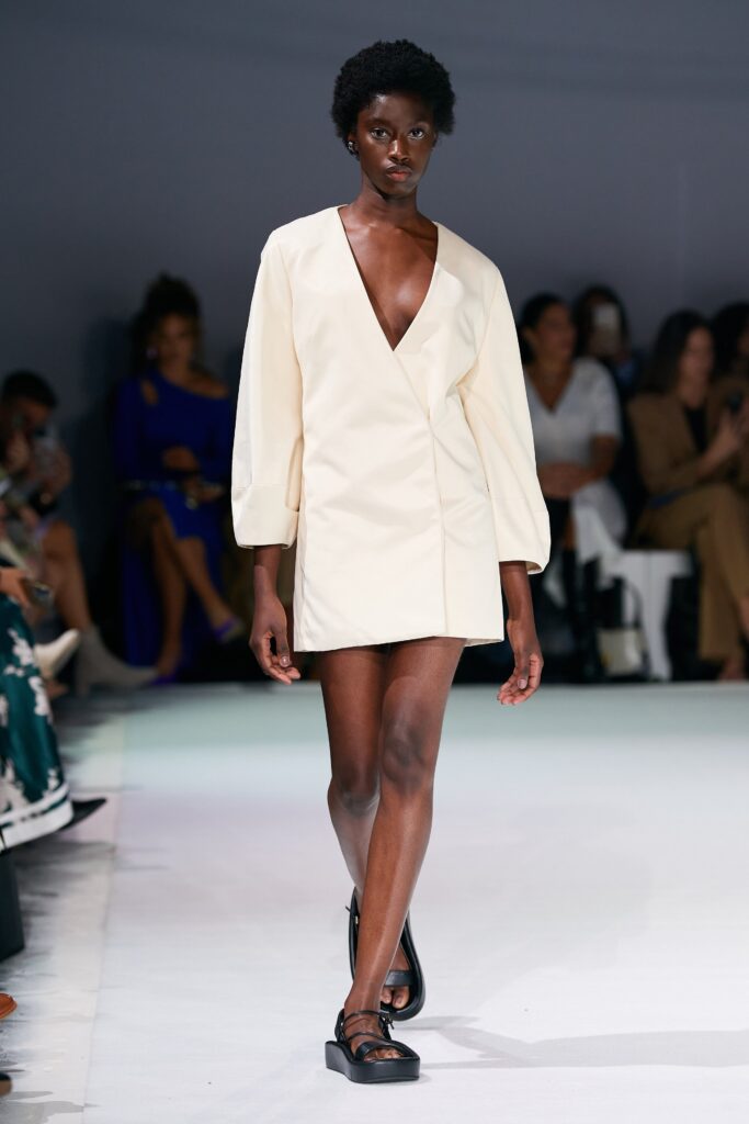 A fitted cream dress with long sleeves and a V-neckline featuring an asymmetric design.