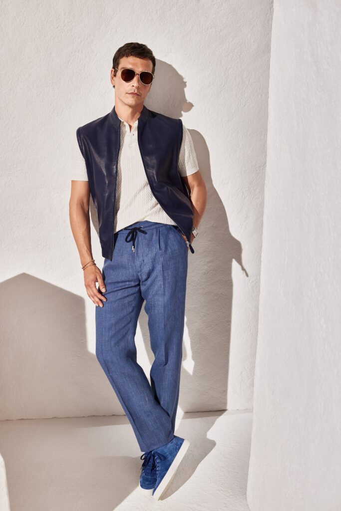 A relaxed fit outfit featuring a sleeveless black leather vest and straight-leg blue cotton pants.