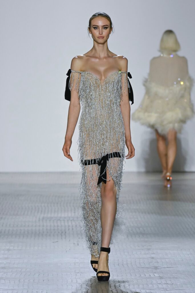 A fitted silver sequined sleeveless dress with a V-neckline and fringed detailing.