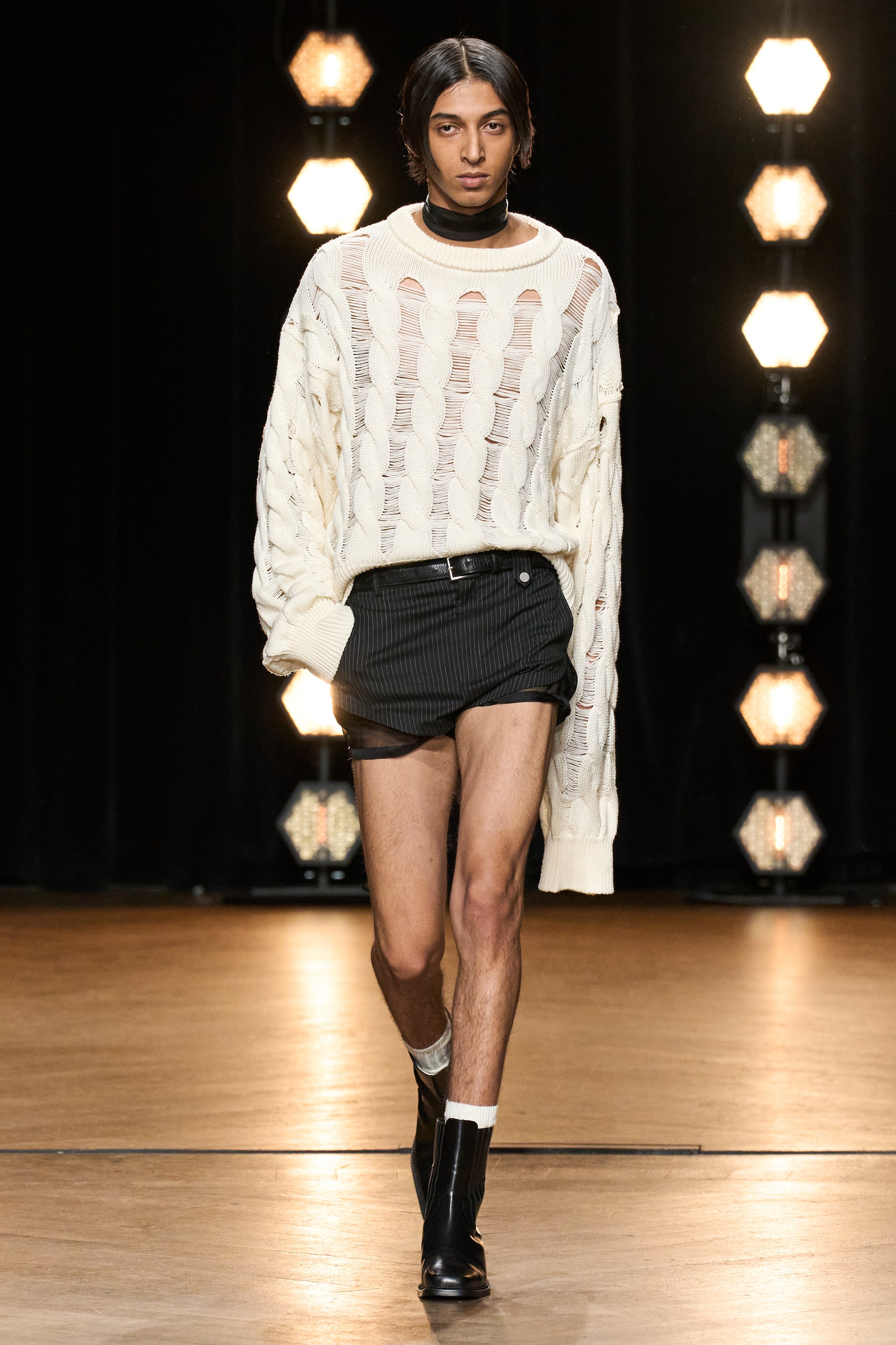 An oversized white sweater with a crew-neck and long sleeves paired with black shorts.
