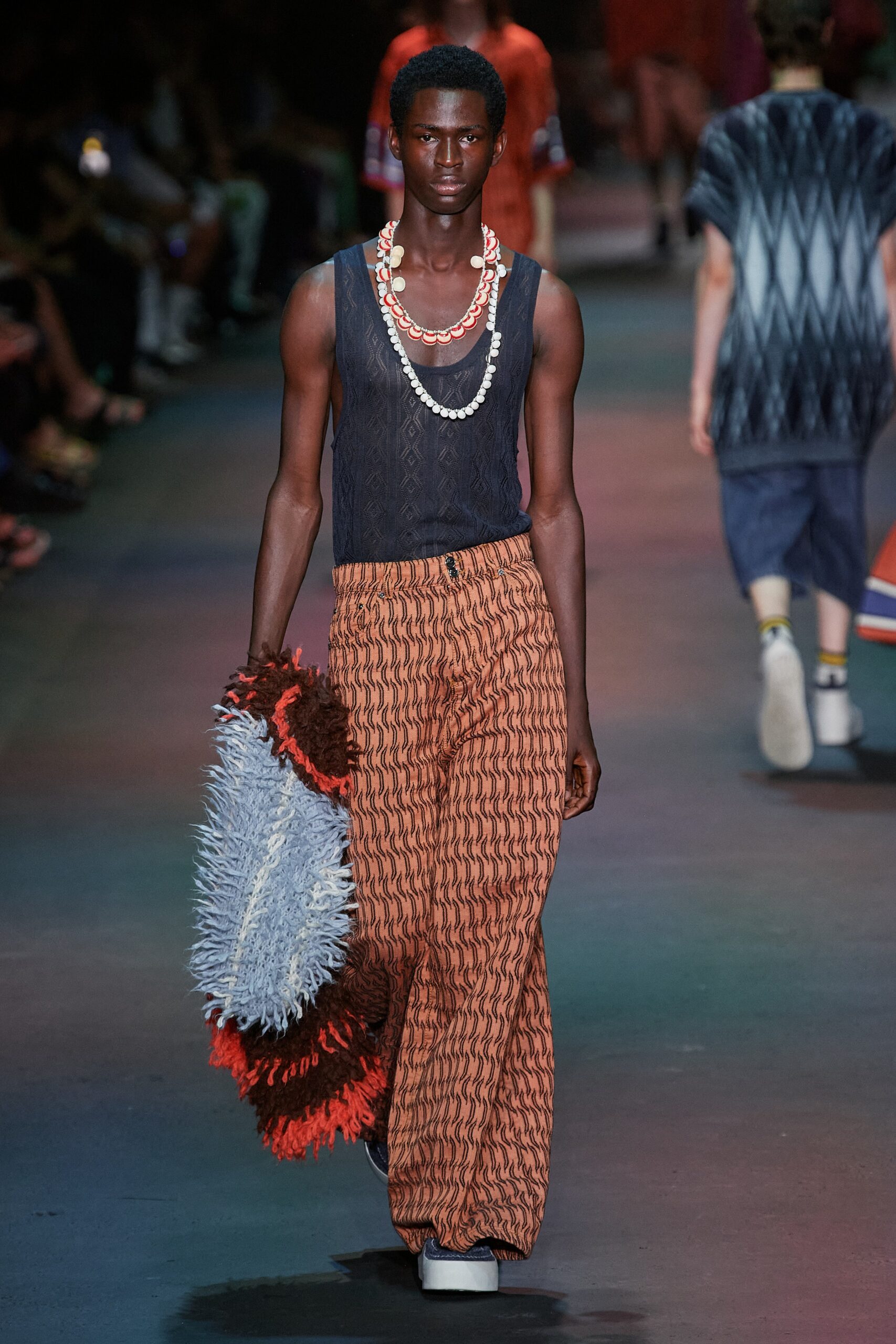 A relaxed black sleeveless top with a high-neck paired with printed wide-leg orange pants.