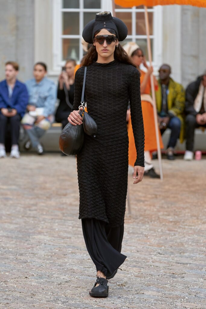 A fitted black dress with long sleeves and a high neckline, paired with straight-leg pants.