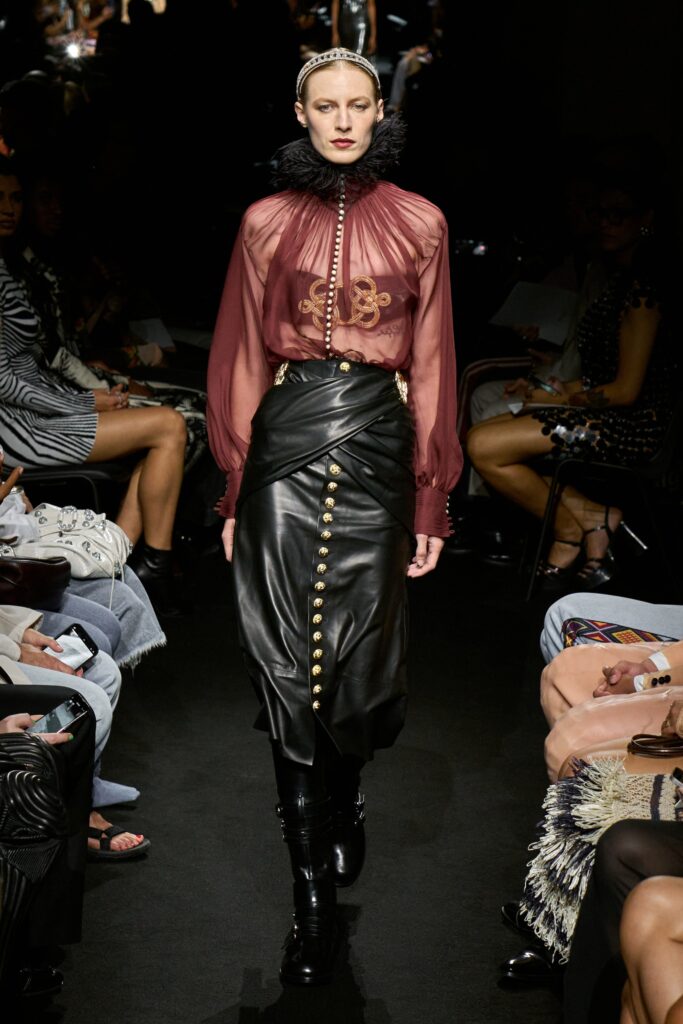 A fitted red blouse with long sleeves and a collared neckline paired with a black leather skirt featuring button details.