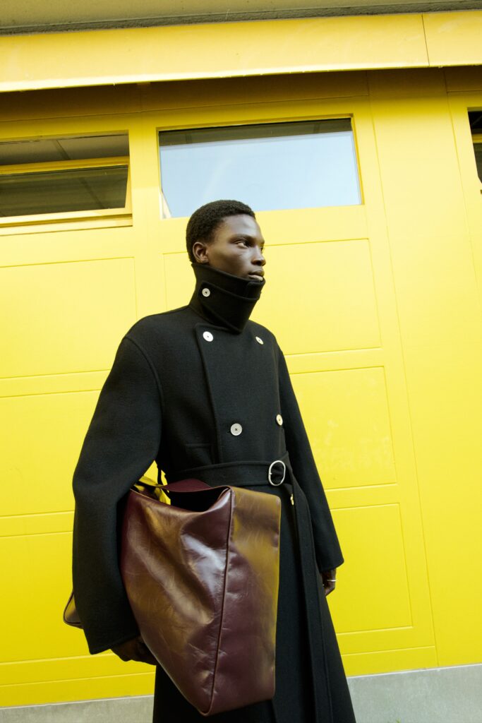 A fitted black wool coat with long sleeves and a collared design, featuring button details.