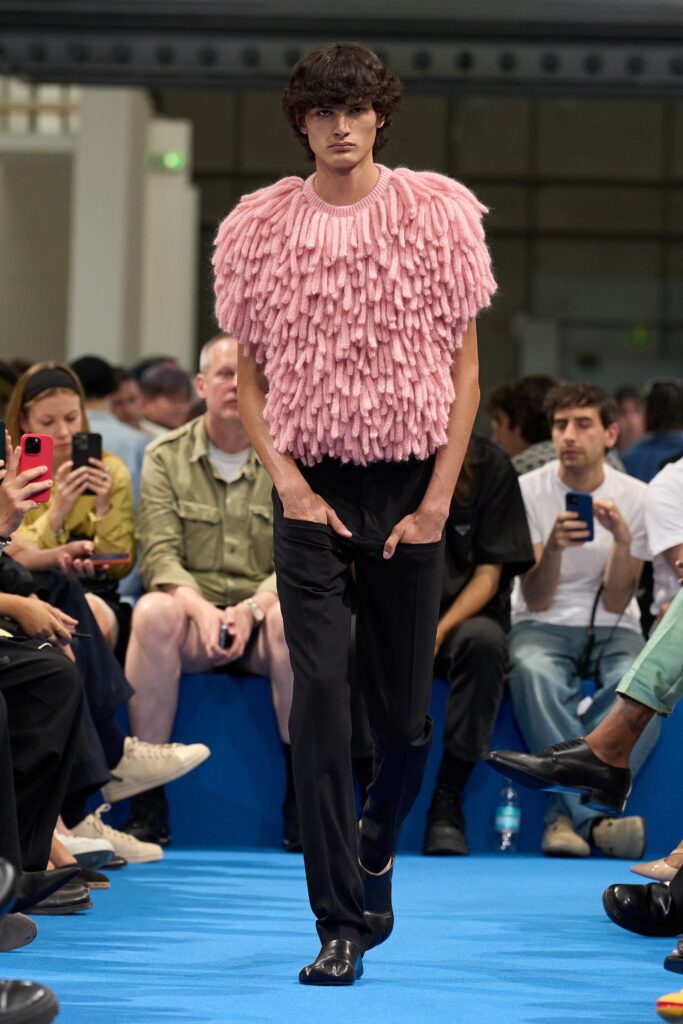 A relaxed pink fringed top paired with black pants, creating a bold fashion statement.