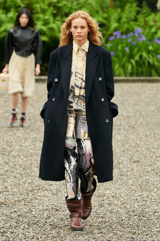 A relaxed black coat paired with multicolor printed pants and a collared shirt.