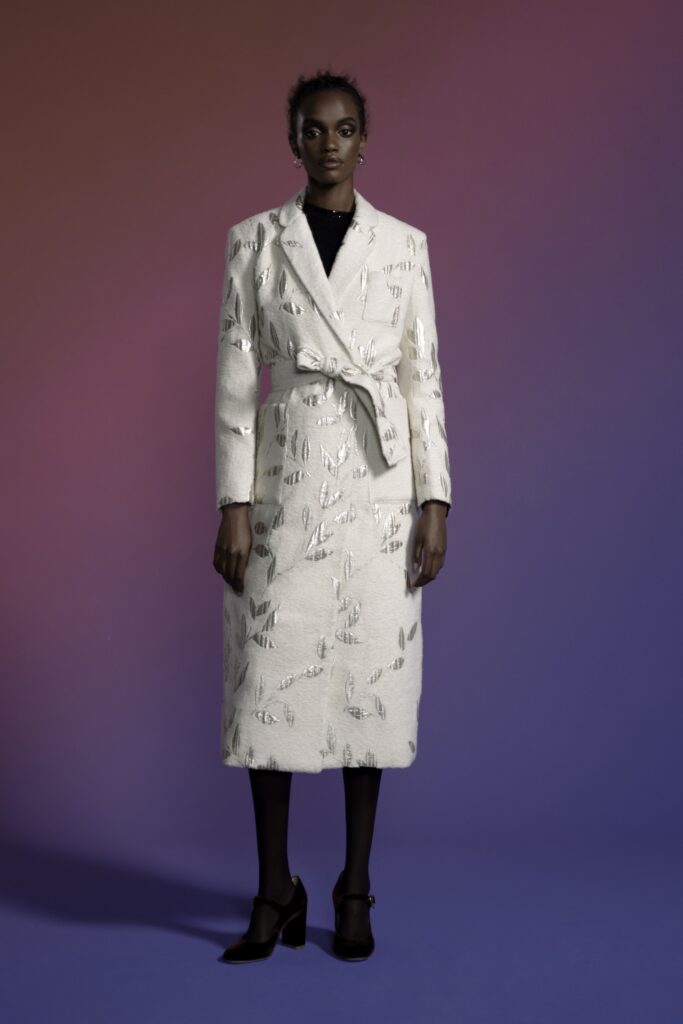 A fitted white silk coat dress with long sleeves, a collared neckline, and embroidered details.