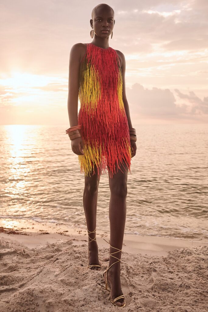 A fitted sleeveless dress with a high neckline, featuring a fringed design in red and yellow.