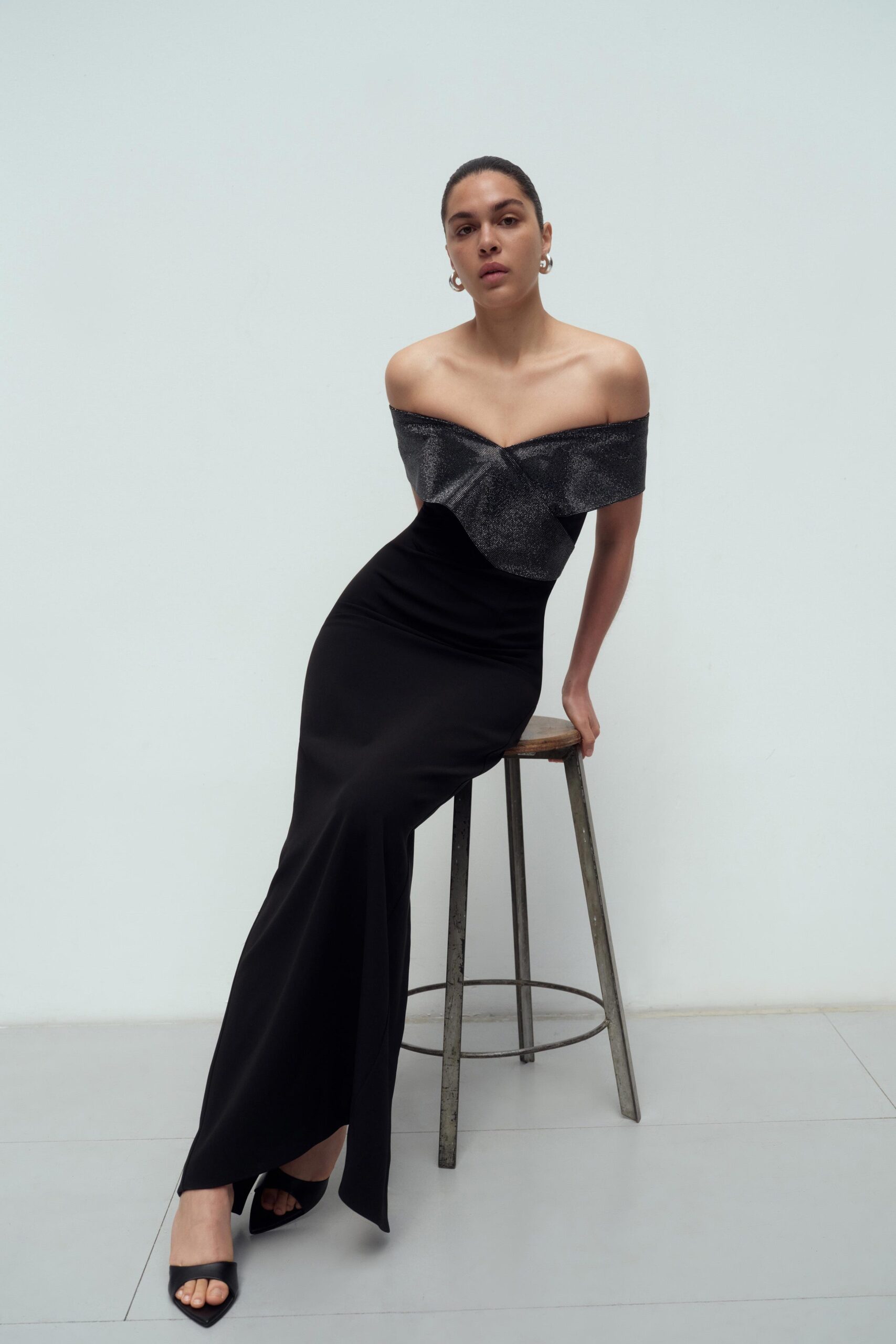 A fitted black silk dress with an off-shoulder design and a stylish slit.