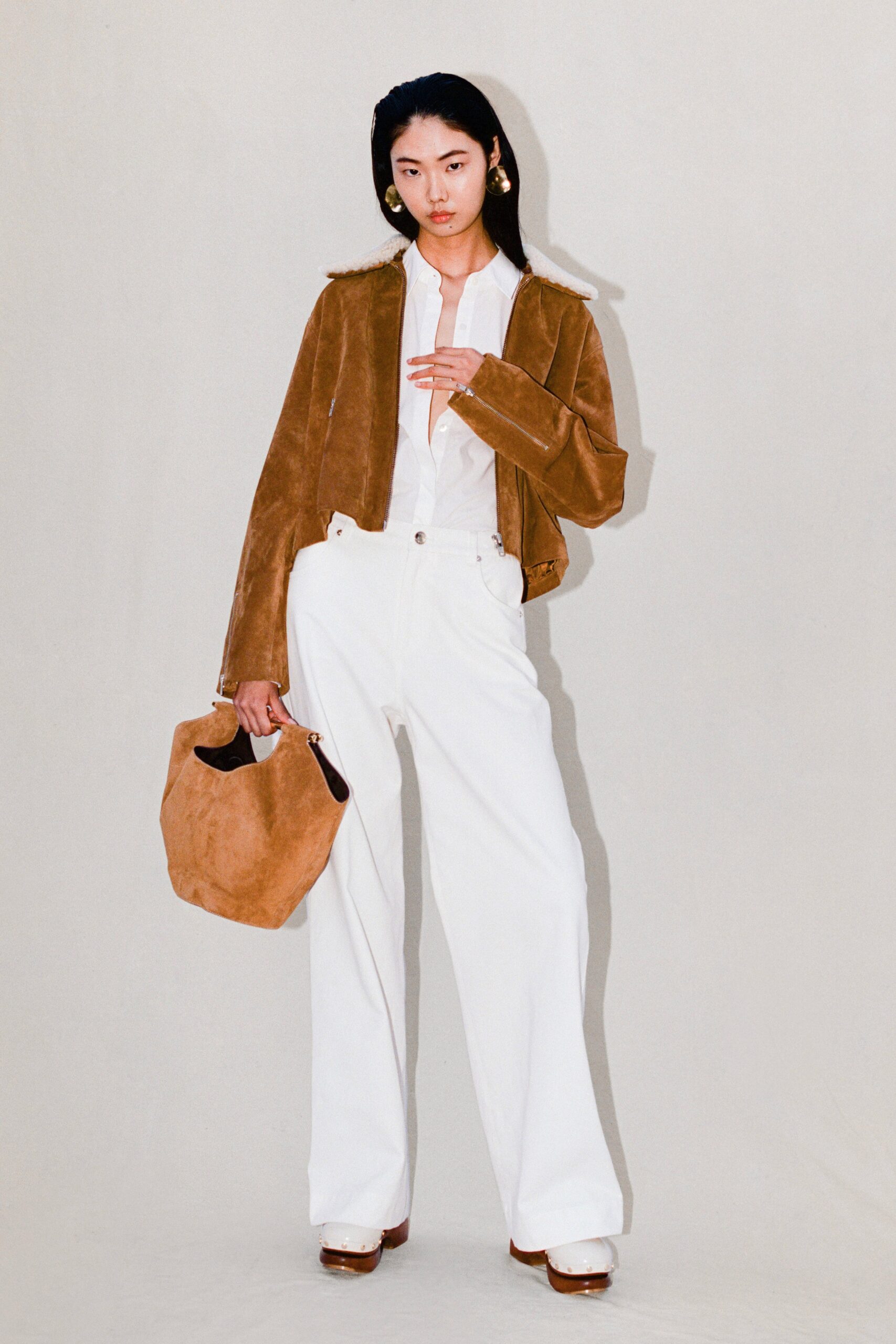 A relaxed brown suede jacket paired with white wide-leg pants and a collared shirt.