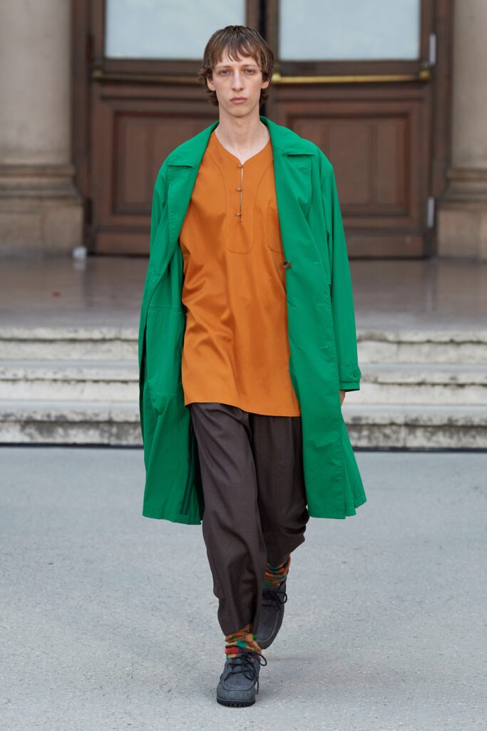 A relaxed green coat layered over an orange top and brown pants.