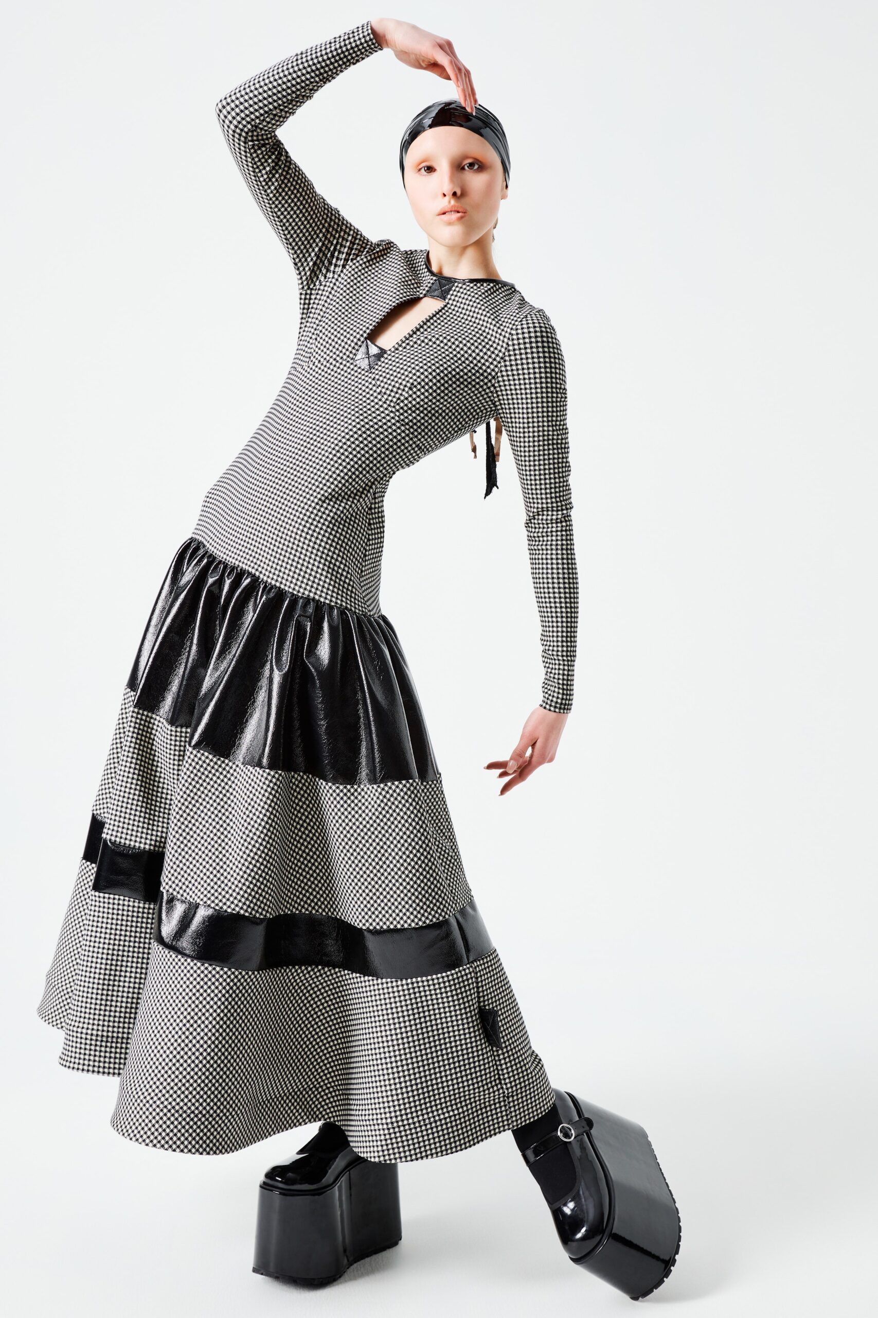 This fitted dress features a striking tiered design, combining a textured black and white pattern with a dramatic silhouette. The long sleeves and V-neckline enhance its contemporary appeal, while the asymmetric layers create movement and visual intrigue.