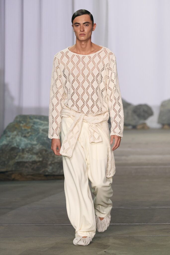 A relaxed white long-sleeve top paired with layered pants for a contemporary look.