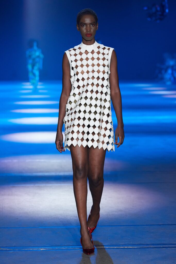 A fitted white sleeveless dress with a high neckline and cutout design.