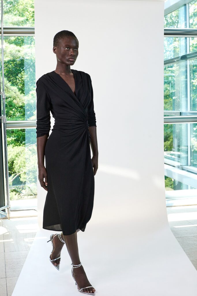 A fitted black dress with long sleeves and a V-neckline featuring a draped design.