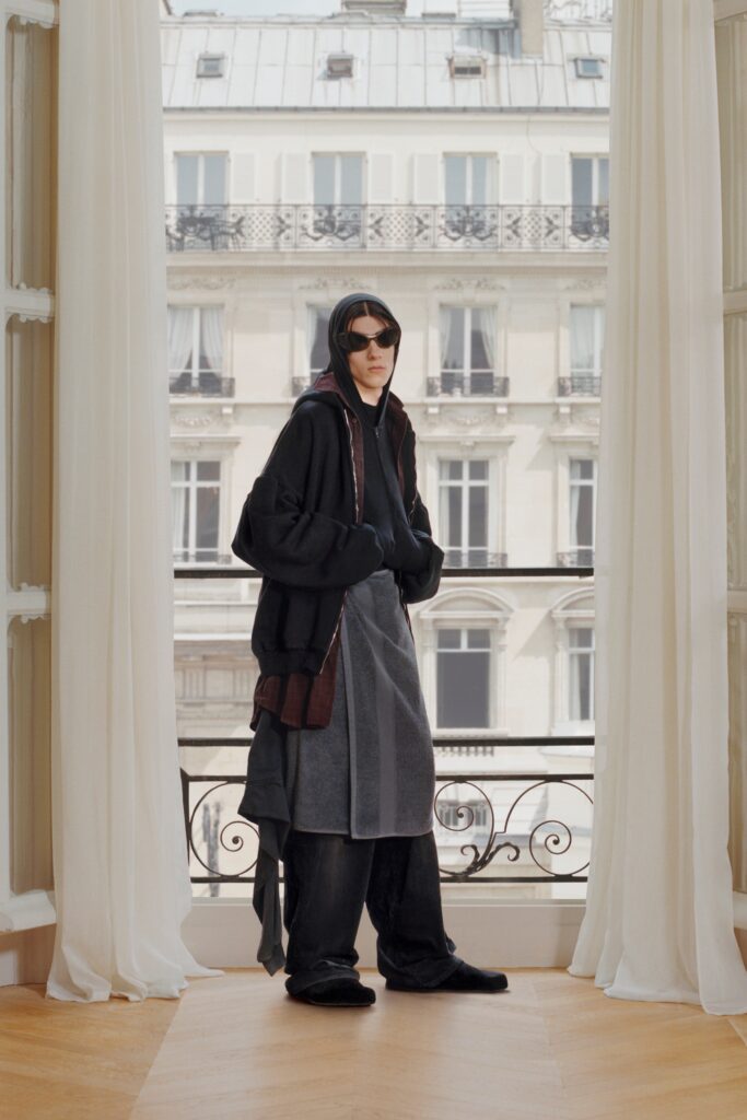 A relaxed black wool coat paired with gray pants, featuring a hood and layered design.