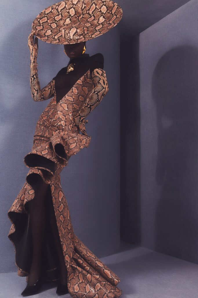 A fitted brown silk dress with long sleeves, a high neckline, and an asymmetric flared design.
