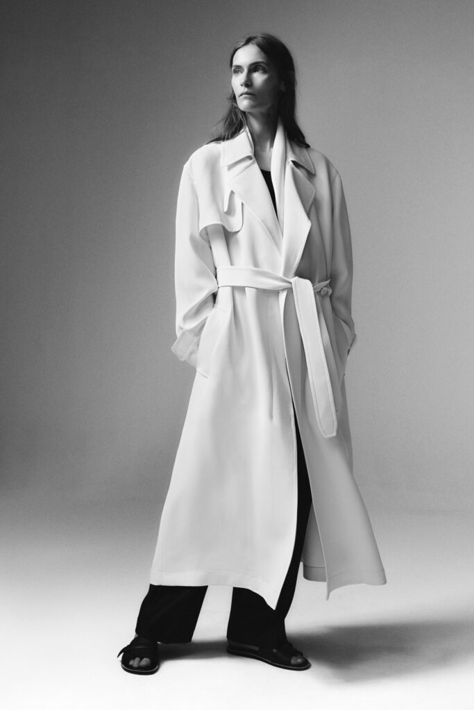 A relaxed white coat with long sleeves, belted at the waist, paired with black pants.