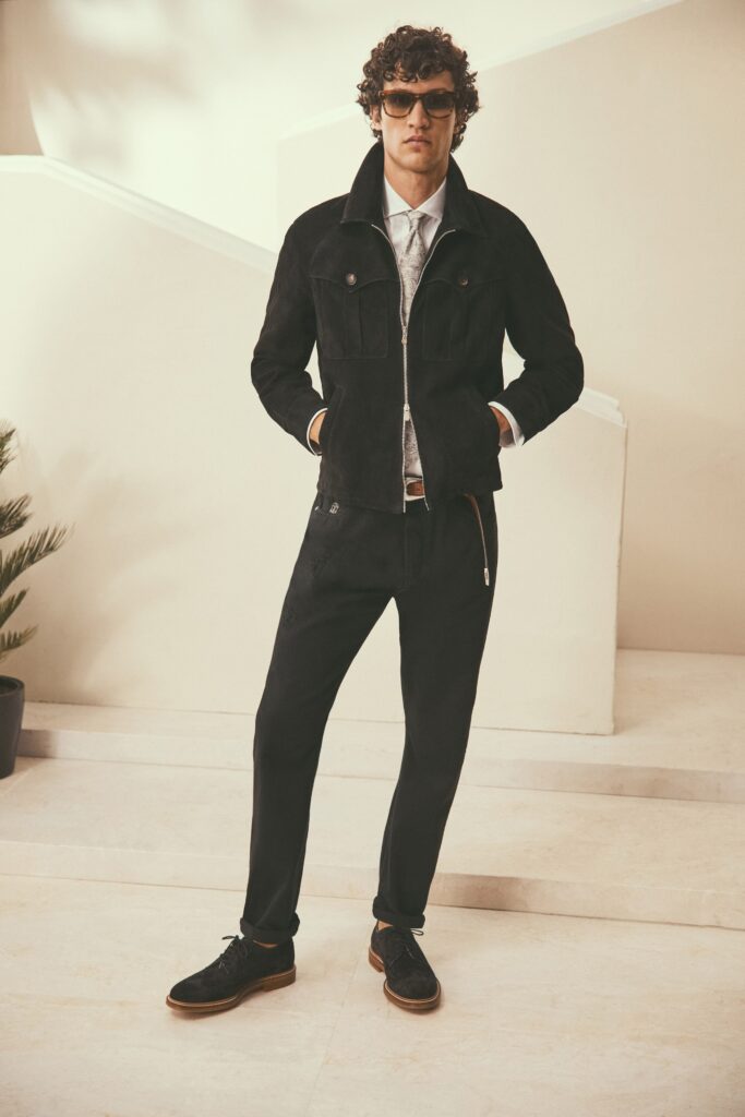A fitted black suede jacket with long sleeves and collared design, paired with tailored black pants.
