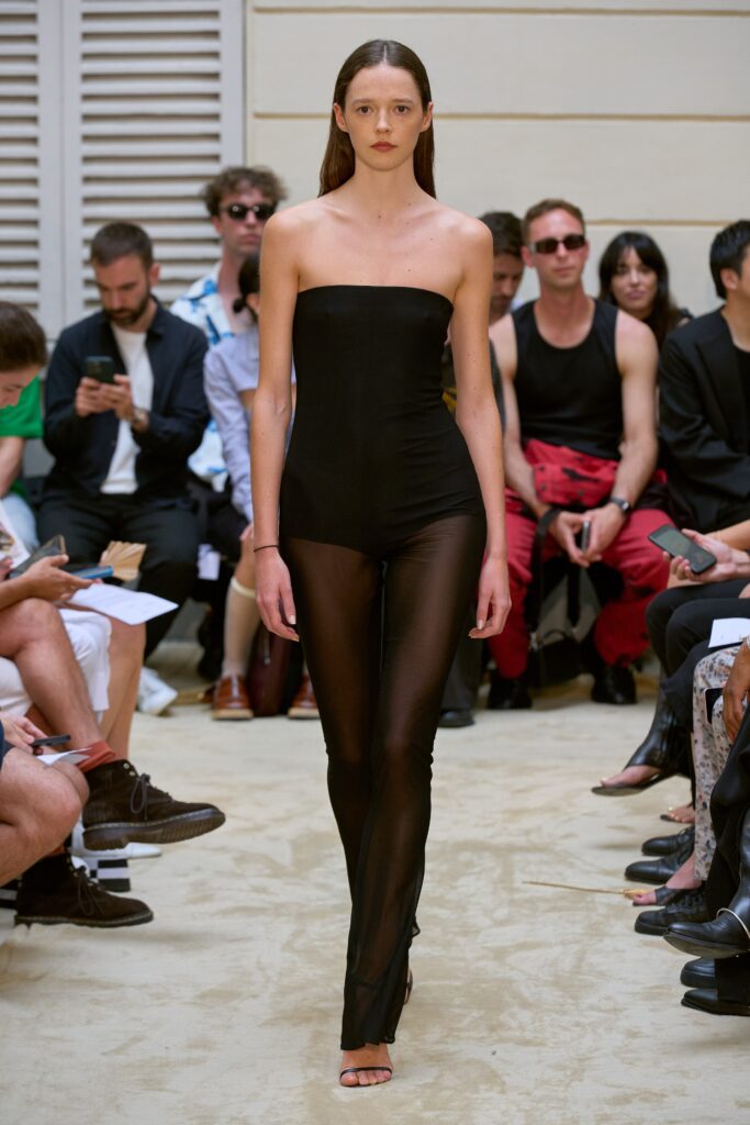 A fitted black sheer catsuit with a sleeveless design and high-neck construction.