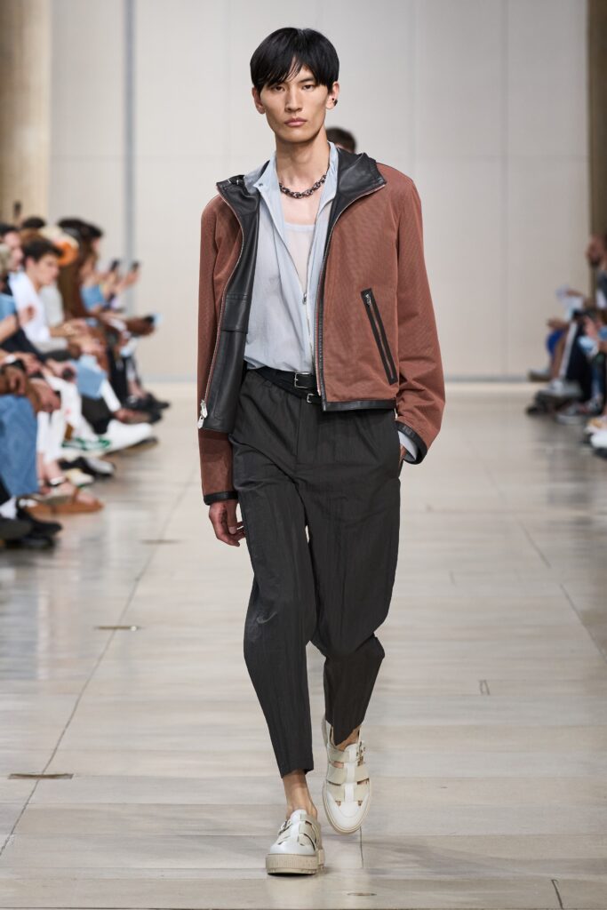 A relaxed brown leather jacket paired with gray pleated pants for a stylish look.