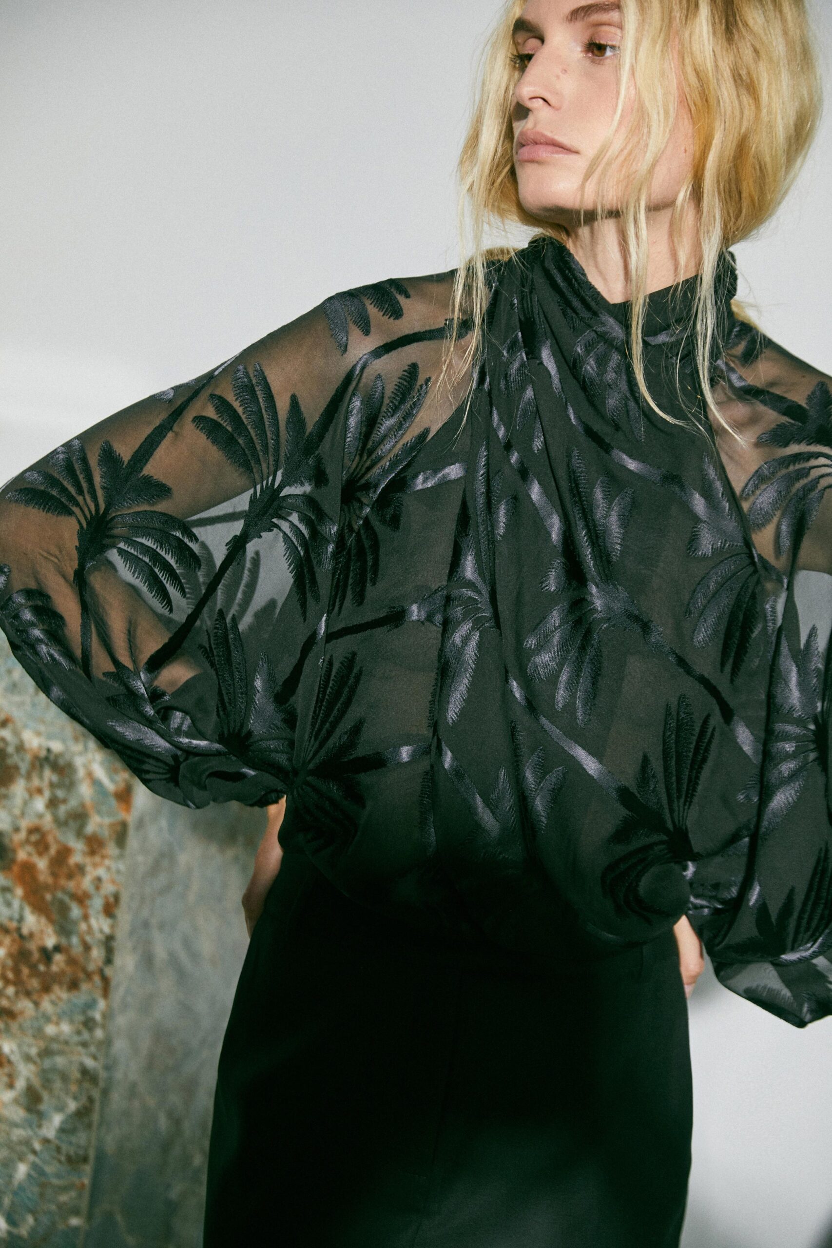 A fitted black silk dress with long sleeves and a high neckline featuring layered details.