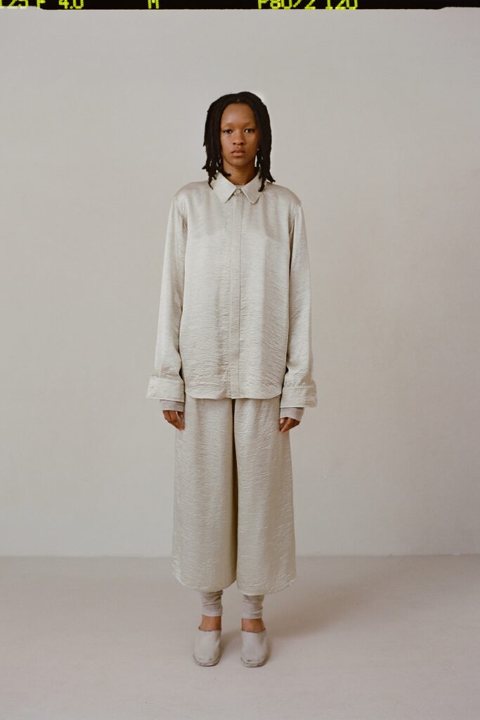 A relaxed beige silk shirt with long sleeves and a collared neckline paired with wide-leg pants.