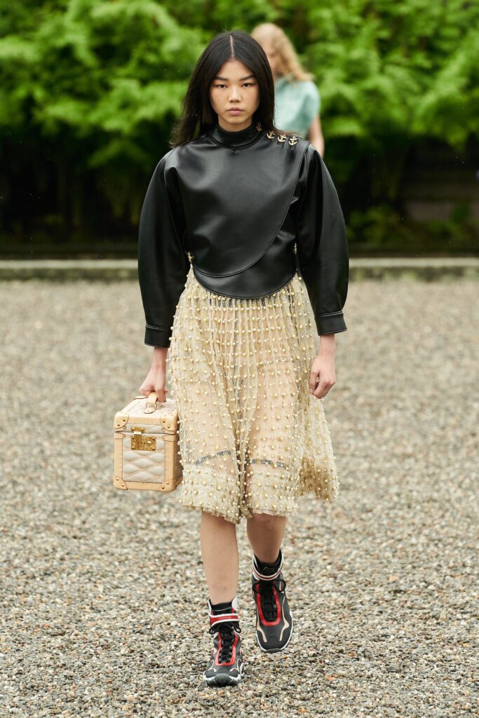 A fitted black leather long-sleeve top paired with a pleated beige skirt.