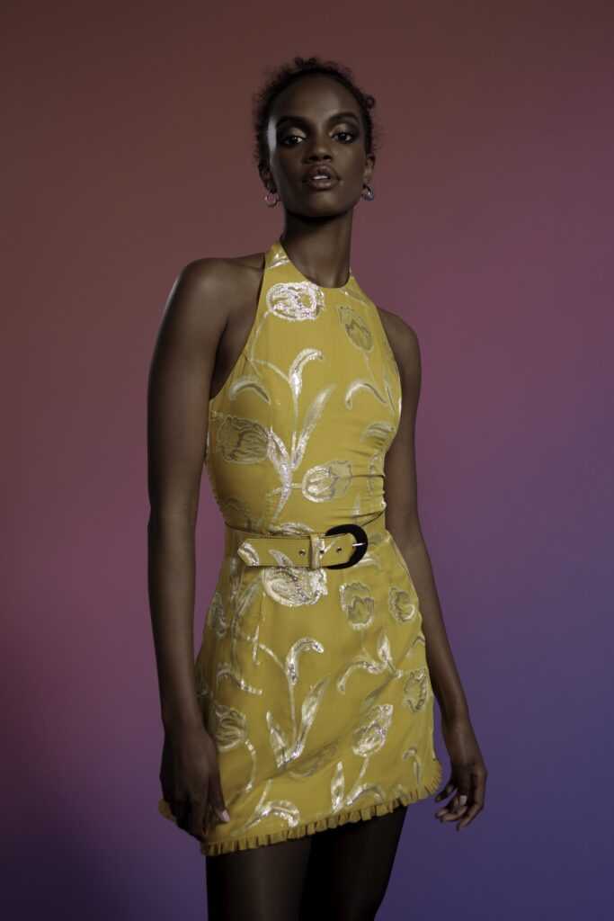 A fitted yellow silk sleeveless dress with a high neckline and mini length, featuring embroidered details.