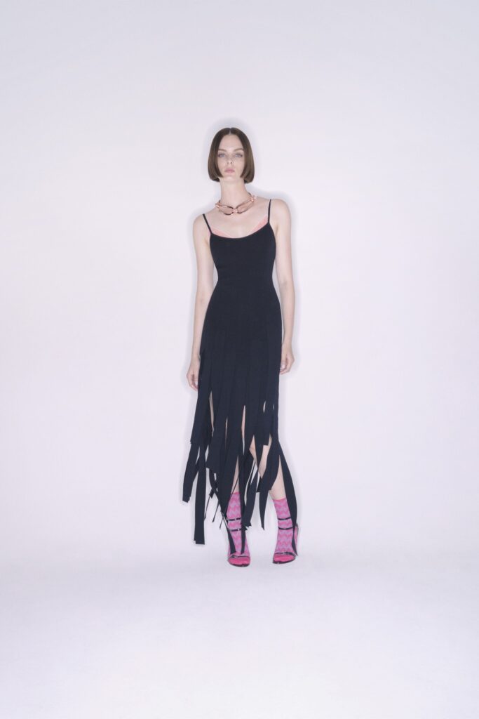 A fitted black sleeveless dress with a V-neckline and asymmetric design details.
