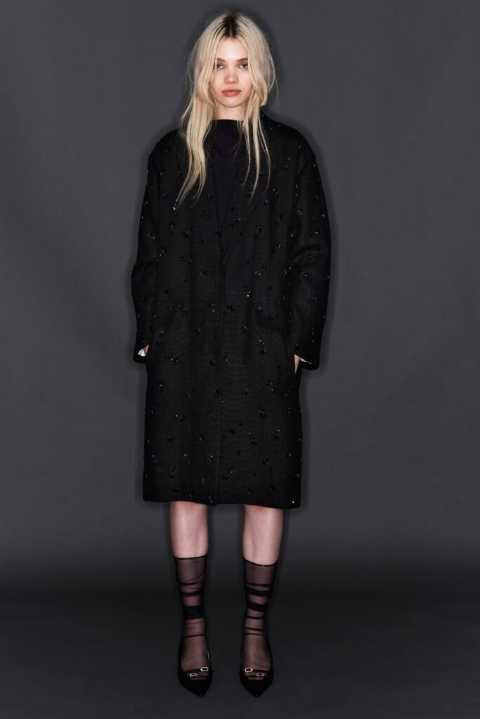 A relaxed black cotton coat with long sleeves and a collared design, featuring button details.