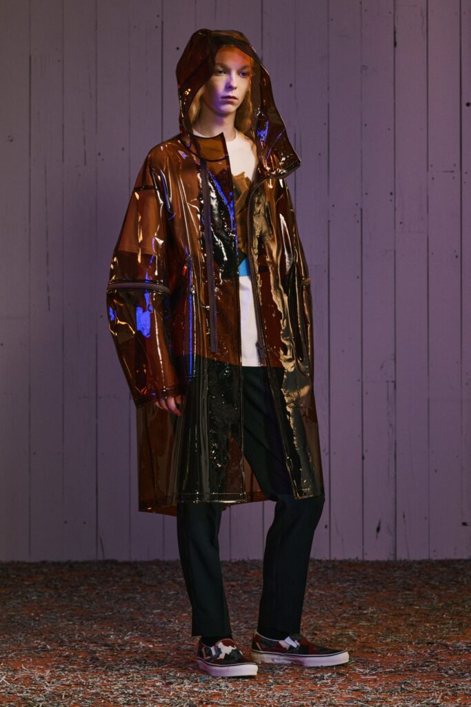 A relaxed brown plastic hooded coat with long sleeves and an asymmetric design.
