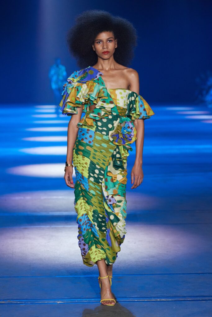 A fitted off-shoulder dress with ruffled details and a vibrant printed design in green, blue, and yellow.