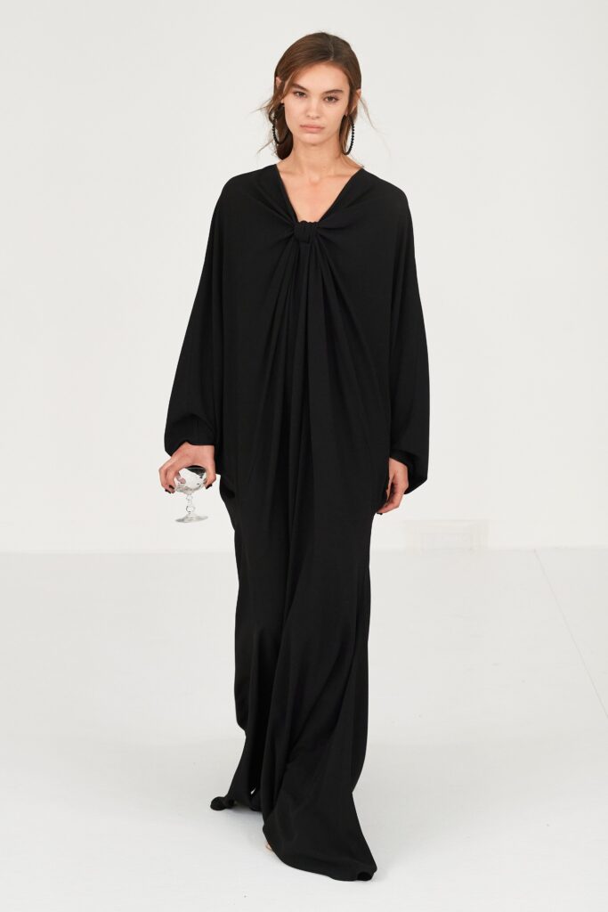 A relaxed black silk dress with long sleeves and a V-neckline featuring a draped design.