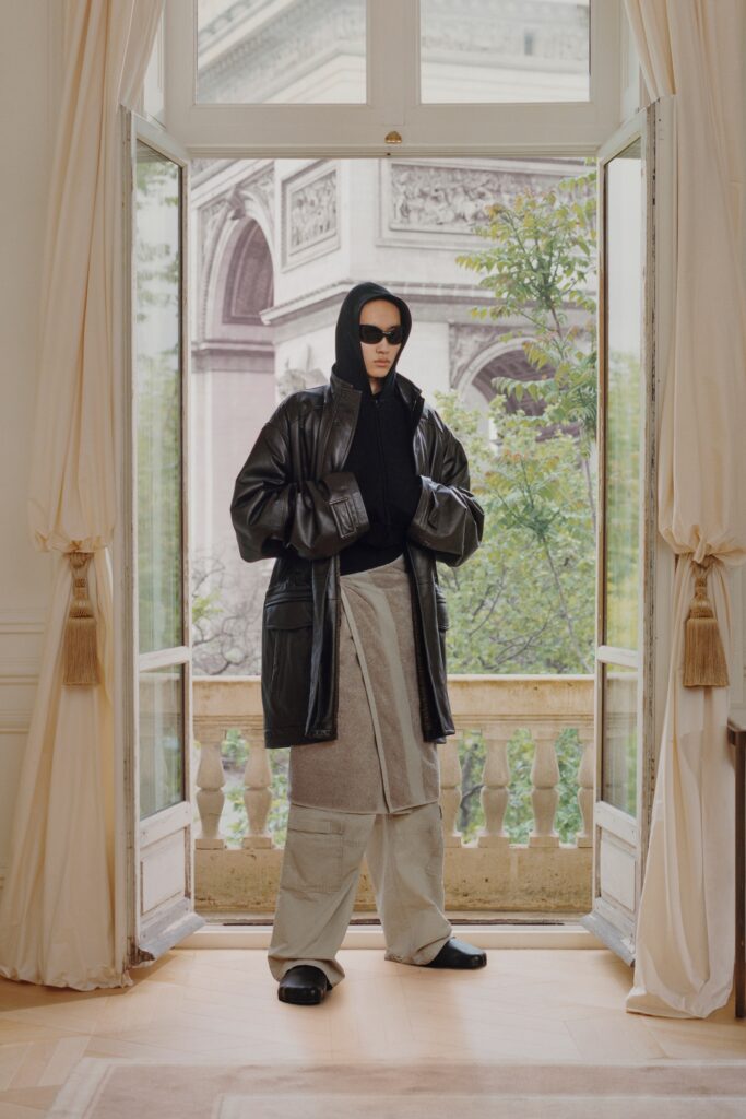 A relaxed black leather coat paired with gray cotton pants, featuring a hood for a contemporary look.