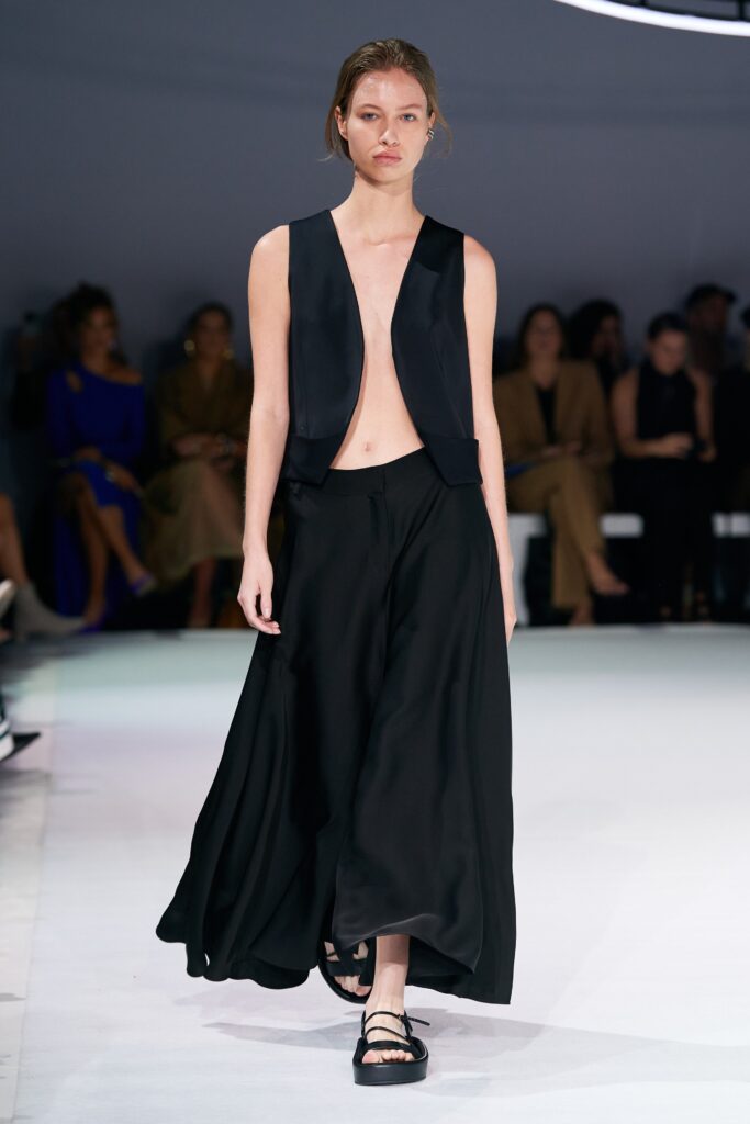 A relaxed black silk sleeveless top with a V-neckline paired with a flared black skirt.