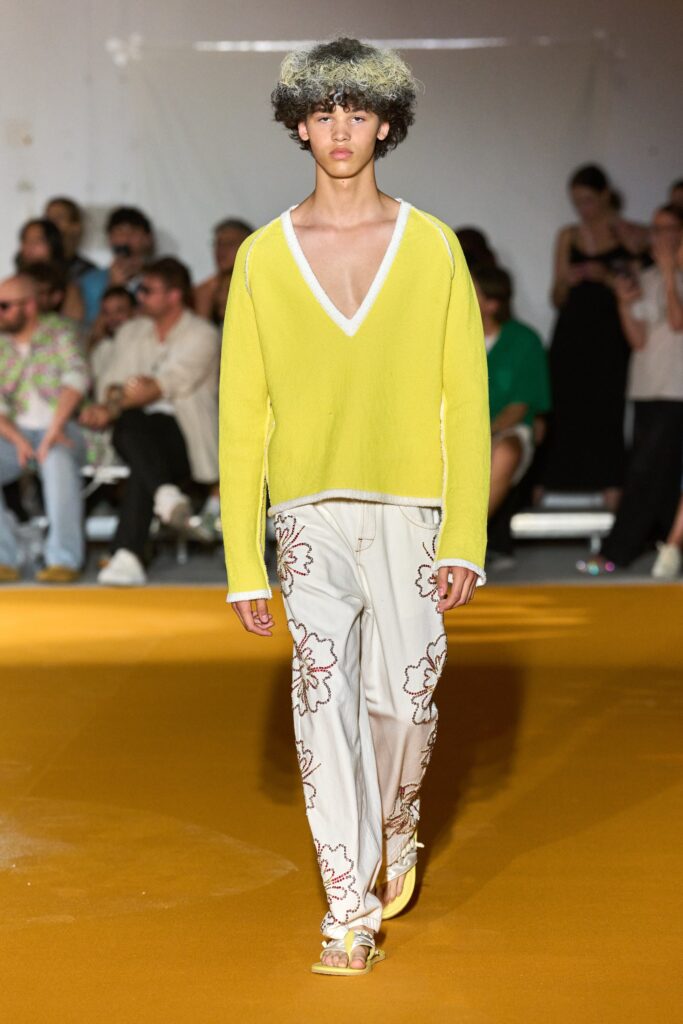 A relaxed yellow long-sleeve sweater with a V-neck paired with white flared pants.