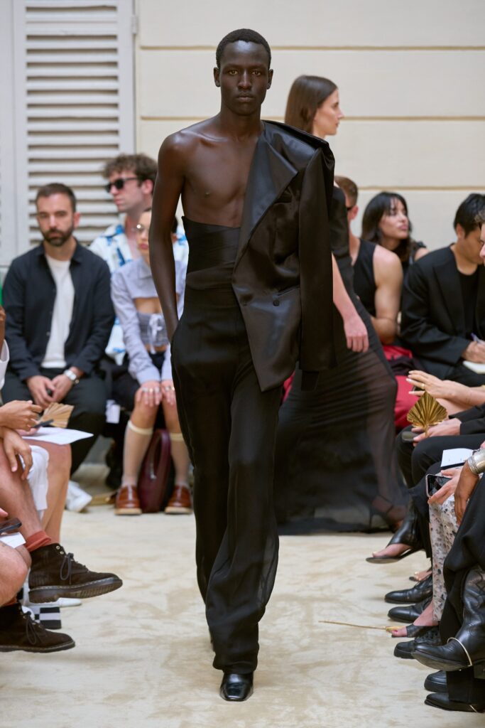 A fitted black silk jacket with an asymmetric design paired with sleek black pants.