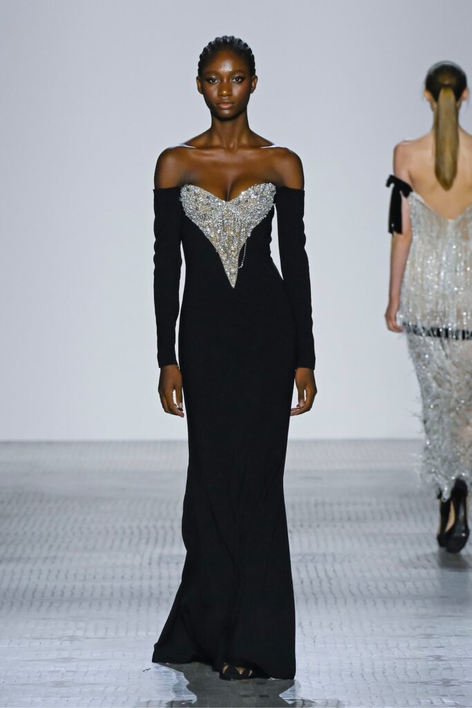A fitted black silk off-shoulder gown with embroidered detailing and long sleeves.