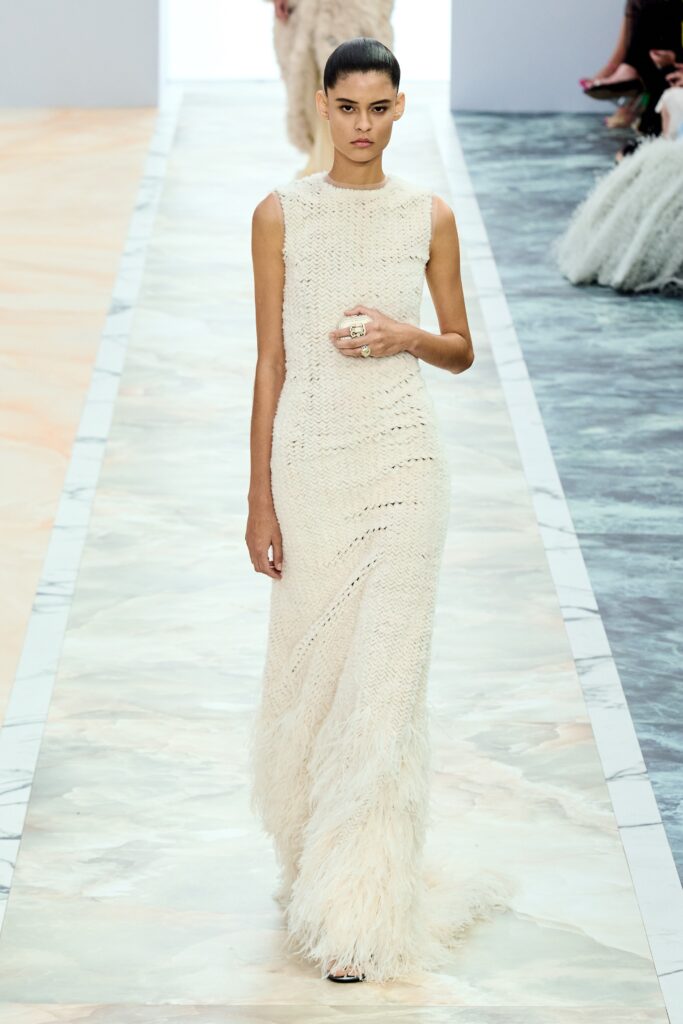 A fitted white sleeveless dress with a high neckline and fringed detailing.