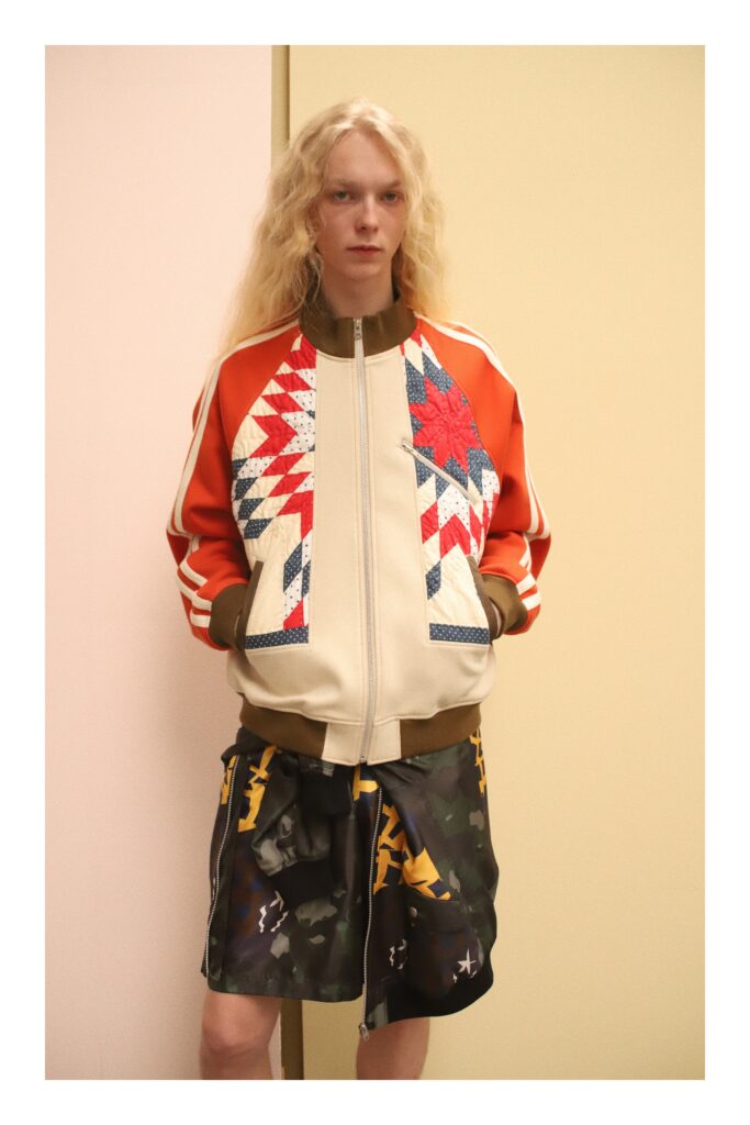 An oversized orange jacket with printed details paired with black camouflage shorts.