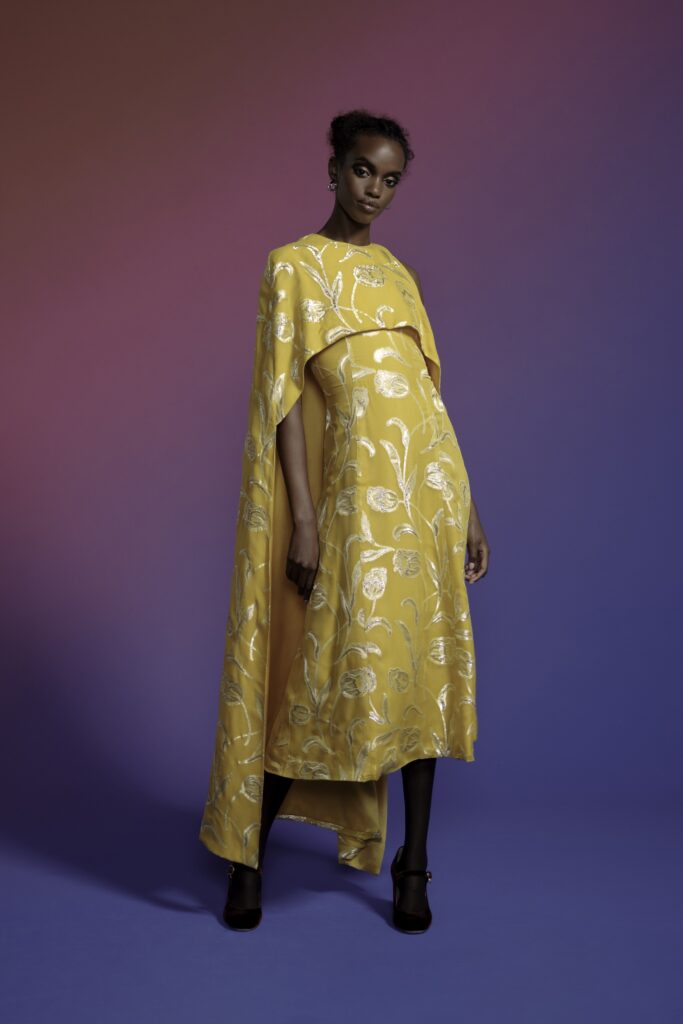 A fitted yellow silk dress with a high-neck and embroidered details, complemented by a matching cape.